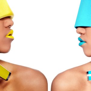 Due modelle con make-up colorato e accessori audaci una di fronte all'altra, simbolo di creatività e soluzioni linguistiche per il settore fashion & luxury.