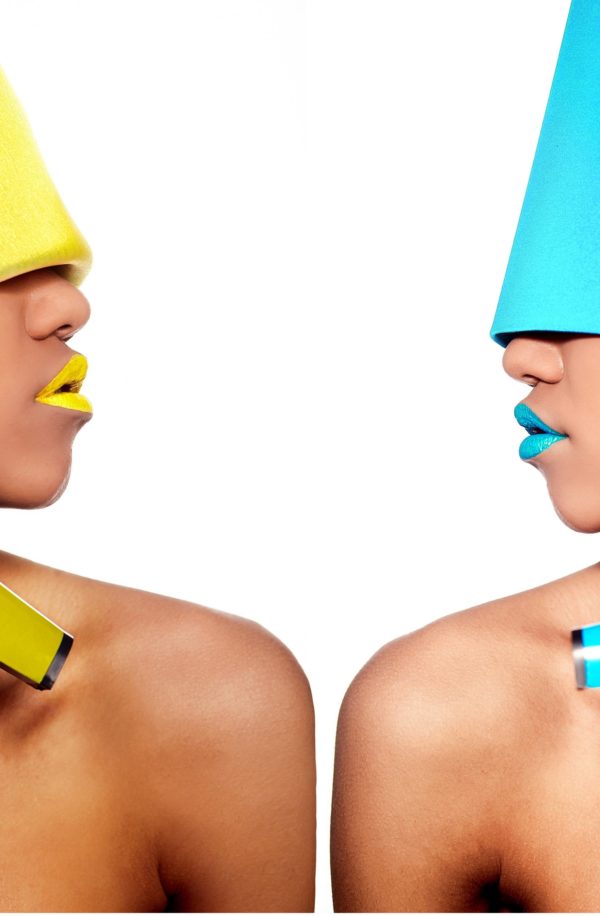 Due modelle con make-up colorato e accessori audaci una di fronte all'altra, simbolo di creatività e soluzioni linguistiche per il settore fashion & luxury.