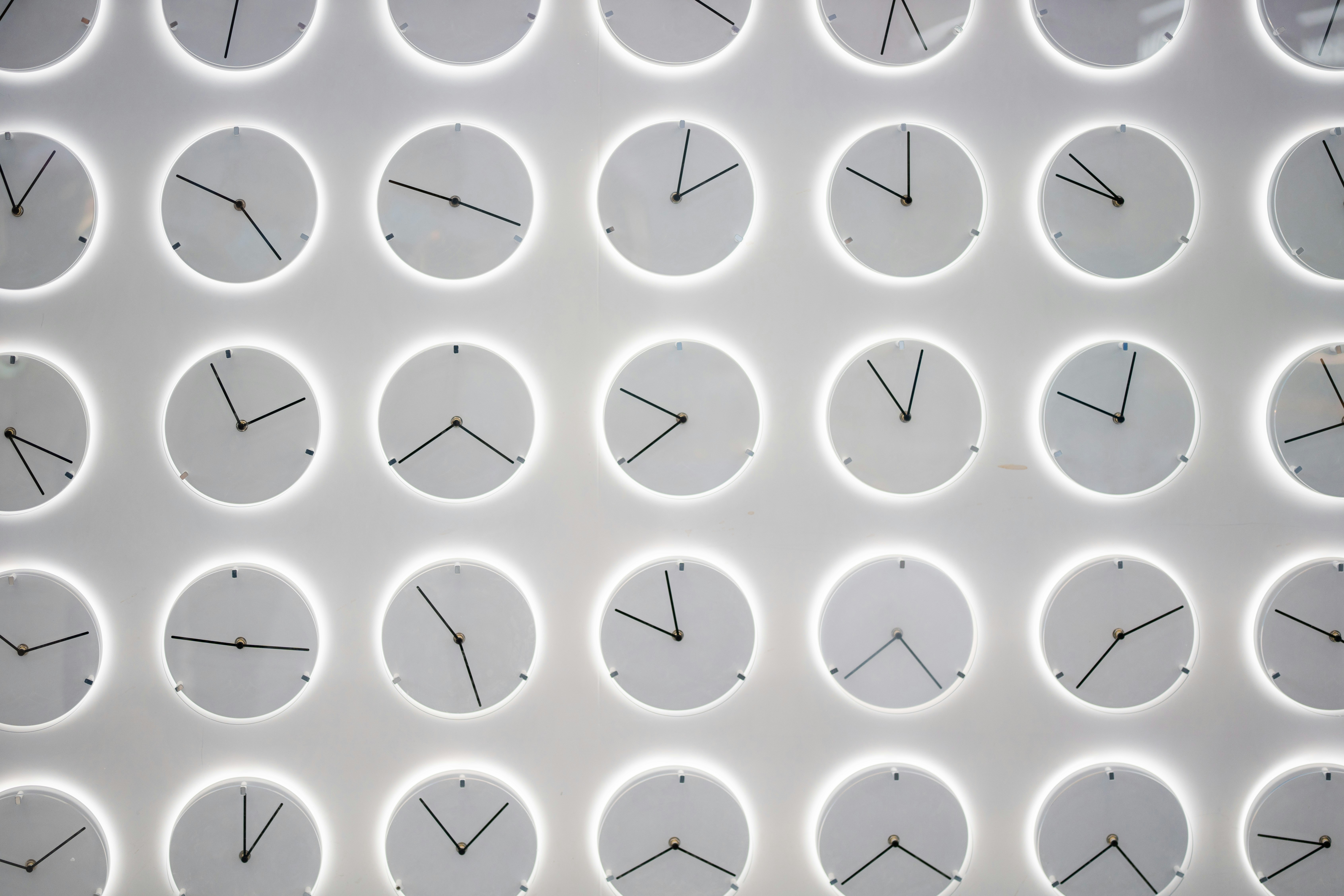 A Wall of white clocks with different times, symbolizing the power of routine and how to optimize your time with good habit management.