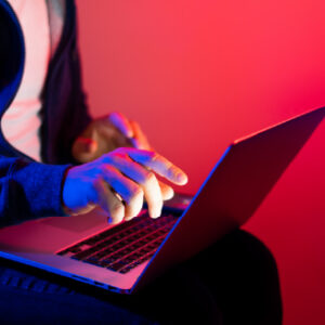 Person in a hoodie using a laptop with blue and red neon lighting