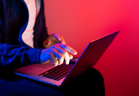 Person in a hoodie using a laptop with blue and red neon lighting