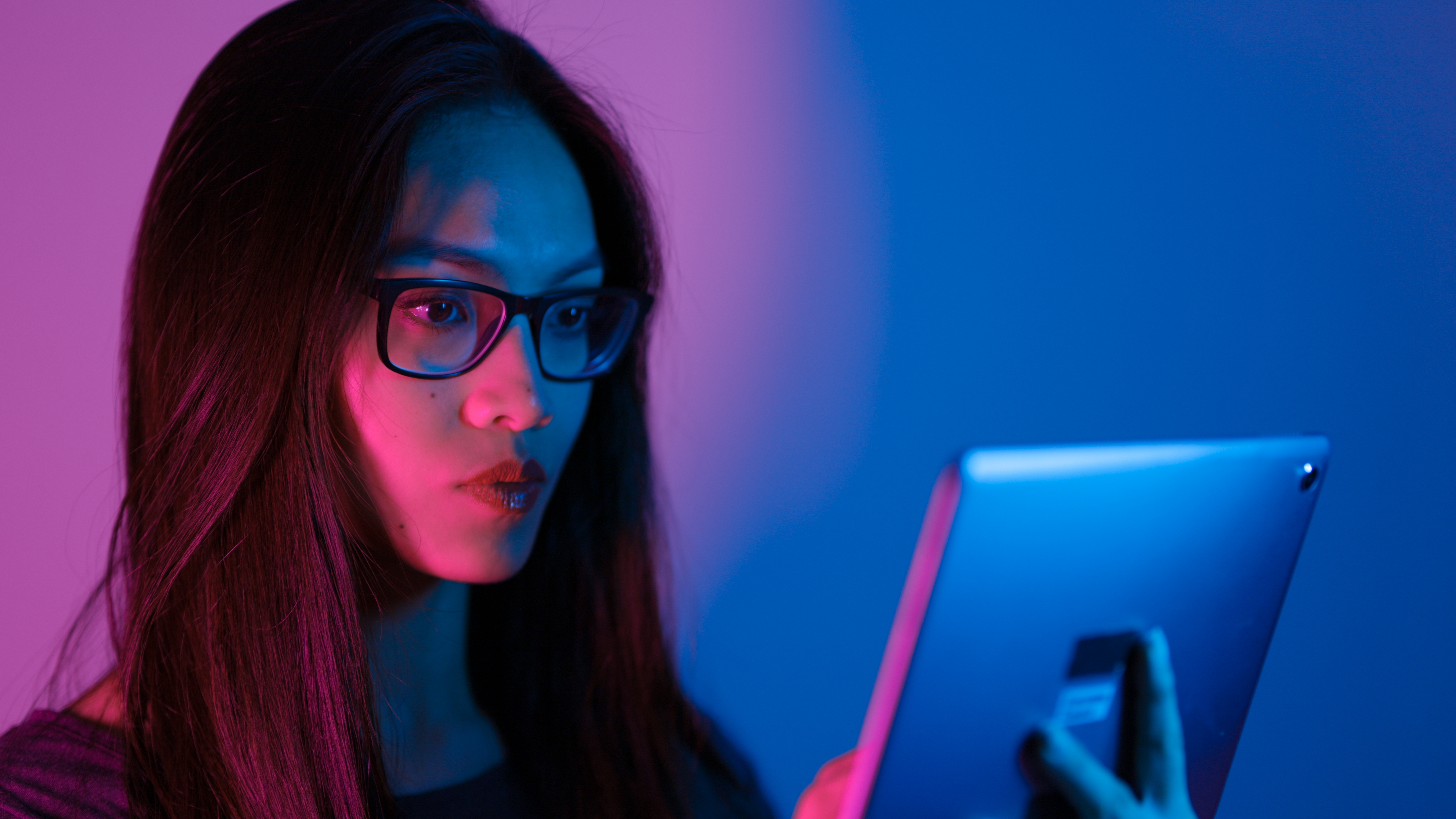 A smart young woman using her device on a neon background