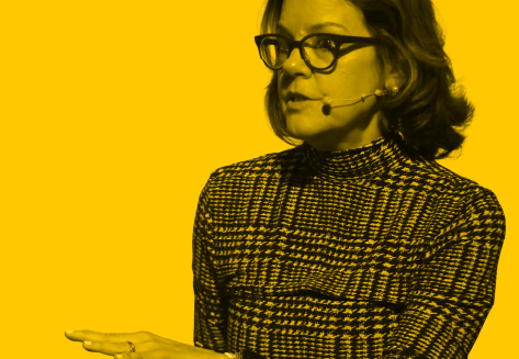 Ann Handley mentre parla all'evento Marketing Forum 2025 , indossando occhiali e maglietta a fantasia, con sfondo a contrasto giallo. Esperta in Marketing e Leader di pensieri in strategie content.
