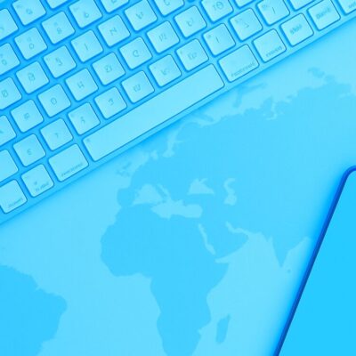 Blue-toned keyboard and smartphone over a world map, for global AI search and international online content